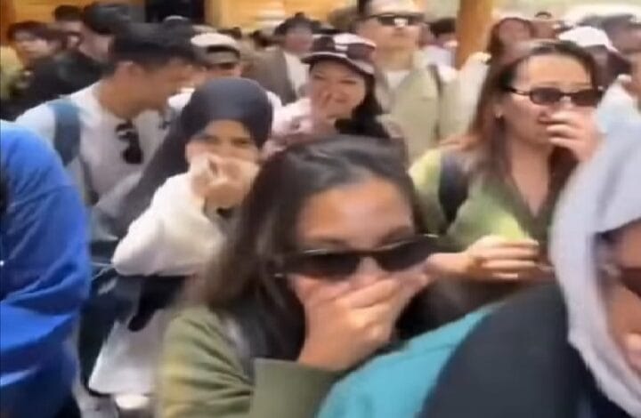 malaysia - Wilayah.com.my Crowded group of people outdoors, some wearing sunglasses or headscarves, many with hands over their mouths as they gaze toward the camera.