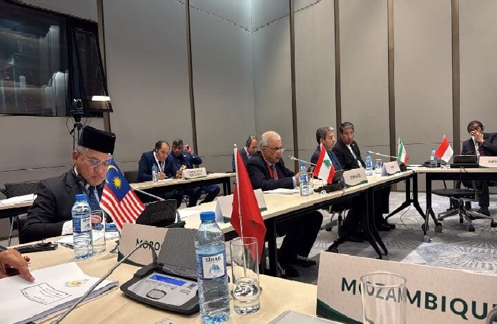International conference room with delegates seated at a long table, multiple national flags visible (Malaysia, Lebanon, Iran, Indonesia, Mozambique).