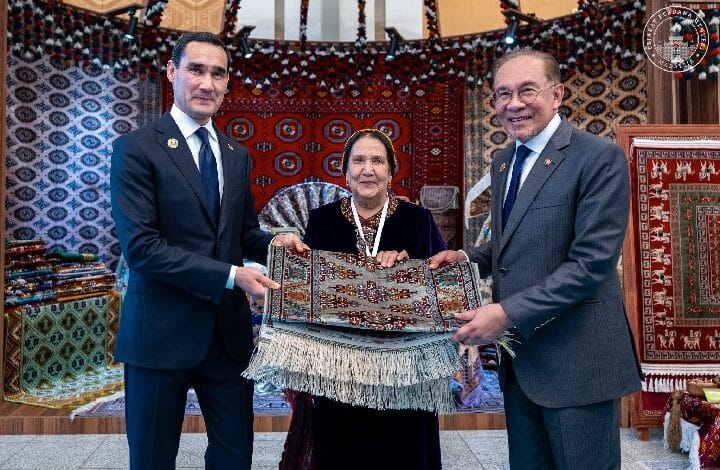 malaysia turkey - Wilayah.com.my Three people in formal attire present a folded decorative rug in a room filled with colorful carpets and patterns.