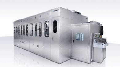 Large stainless steel automated production line with multiple panel doors and windowed access points on a white reflective surface.