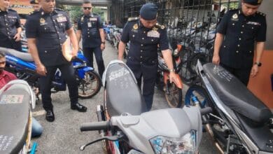 Group of uniformed police officers inspecting parked motorcycles in a fenced area; one officer leans over a bike while others observe.