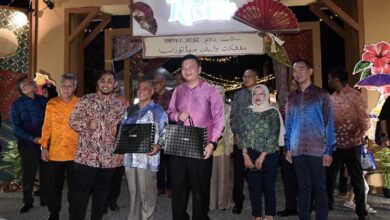 Group of people posing with gift bags at a festive night event under string lights.