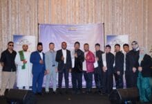 nasyid - Wilayah.com.my Group of men and women in formal attire posing on a stage with a purple backdrop at an event.