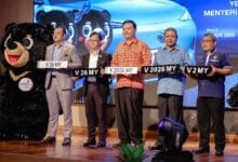 no plate 2 - Wilayah.com.my Six men on a stage holding novelty license plates, with a bear mascot on the left and a blue car backdrop.