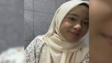 nursayyida - Wilayah.com.my Young woman wearing a cream hijab and floral blouse smiles at the camera against a tiled wall.