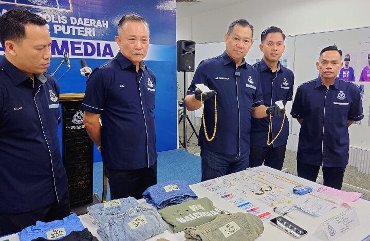 pdrm johot - Wilayah.com.my Five uniformed police officers stand behind a table of seized clothes and jewelry at a media briefing.