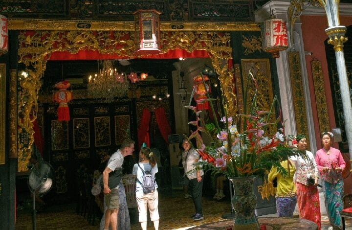 Ornate temple doorway with gold carvings and red drapes, visitors standing inside the entrance.