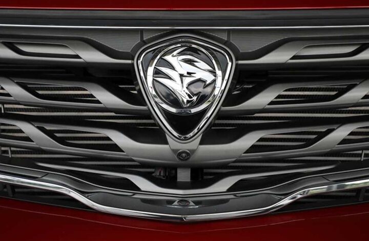 proton - Wilayah.com.my Front grille of a red car with a chrome shield-shaped emblem centered on the grille.