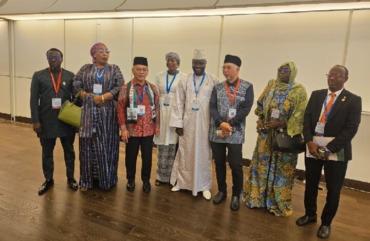 Eight people in formal and traditional attire with conference badges stand in a line inside a conference hall, posing for a group photo.
