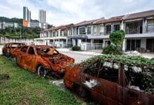 putra height 2 - Wilayah.com.my Two burned-out cars sit on a grassy patch beside a row of damaged townhouses after a fire ruin, with burnt shells and charred windows visible.