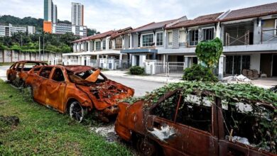putra height 2 - Wilayah.com.my Two burned-out cars sit on a grassy patch beside a row of damaged townhouses after a fire ruin, with burnt shells and charred windows visible.