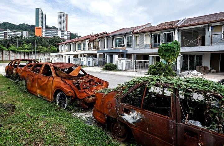putra height 2 - Wilayah.com.my Two burned-out cars sit on a grassy patch beside a row of damaged townhouses after a fire ruin, with burnt shells and charred windows visible.