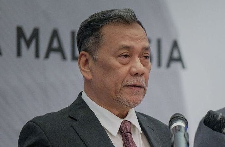 Asian man in a dark suit and pink tie speaks at a podium with two microphones during a press conference.