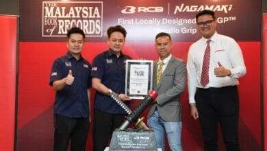 rcb 2 - Wilayah.com.my Four men pose on a red stage, holding a certificate and a large handle grip trophy for a locally designed MotoGP handle grip.