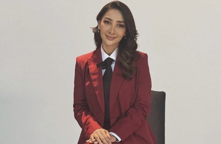 rita rudaini - Wilayah.com.my Professional portrait of a woman in a burgundy blazer and black tie seated against a light background, facing the camera.