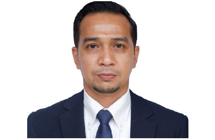 Professional headshot of a man in a navy suit, white shirt, and blue tie against a white background.