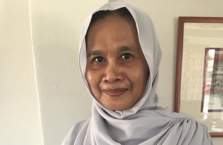 Smiling woman wearing a light gray hijab indoors, facing the camera.