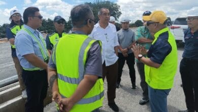 Group of workers and managers in high-visibility vests listening to a man in a white shirt on a construction site.