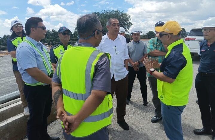 Group of workers and managers in high-visibility vests listening to a man in a white shirt on a construction site.