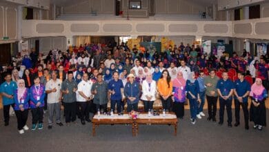 shopee - Wilayah.com.my Large group of people posing for a group photo in a conference hall with a long table at the front and audience seating behind them.
