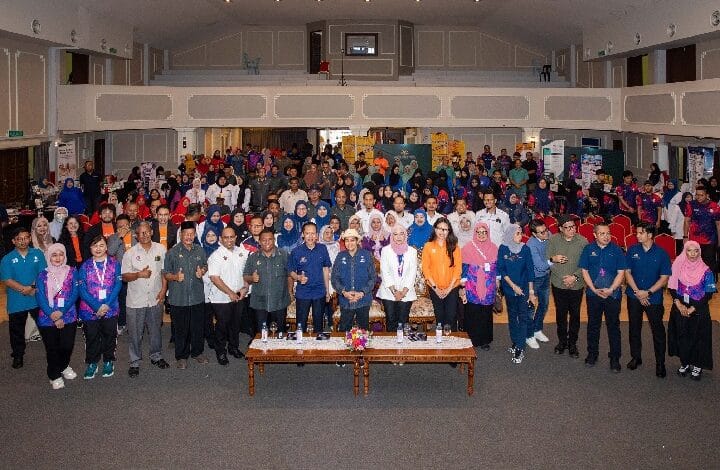 shopee - Wilayah.com.my Large group of people posing for a group photo in a conference hall with a long table at the front and audience seating behind them.