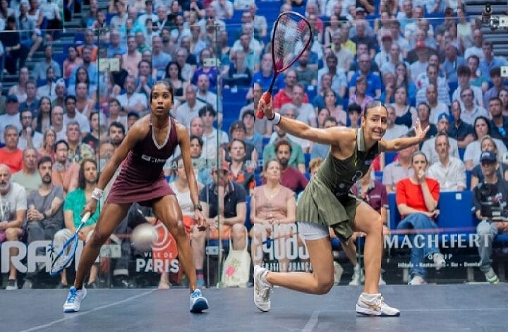 sivasangari - Wilayah.com.my Two female squash players sprint toward the ball on a crowded arena court, racquets raised, mid-match action amid spectators.