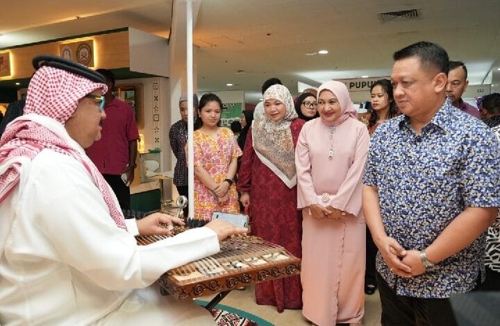 Man in traditional dress plays a qanun for a group of visitors, including women in hijabs, at a cultural event.