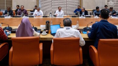 teraju 2 - Wilayah.com.my Officials sit around a long conference table in a formal meeting, viewed from behind three orange chairs in the foreground.