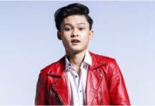 zaki yamani - Wilayah.com.my Portrait of a young man in a red leather jacket and white shirt, posing in a studio with a light blue background.