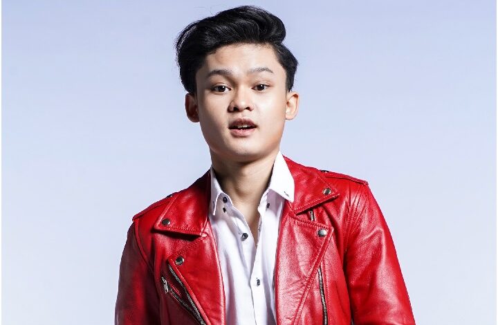 zaki yamani - Wilayah.com.my Portrait of a young man in a red leather jacket and white shirt, posing in a studio with a light blue background.