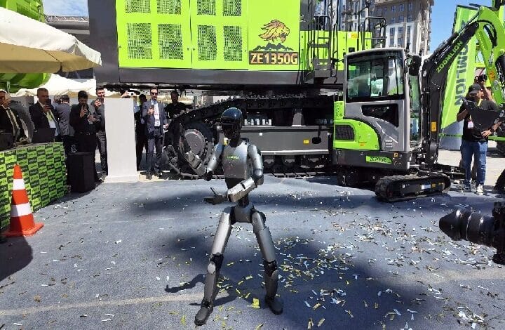 Humanoid robot performing in a plaza during a construction equipment launch, with a bright green excavator and onlookers in the background.