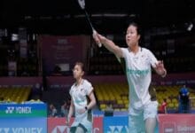 zu ya 2 - Wilayah.com.my Two female badminton players in white Petronas uniforms on a court; one prepares to spike the shuttle while the other watches closely.