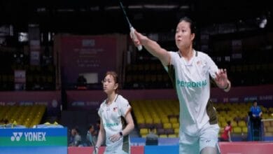 zu ya 2 - Wilayah.com.my Two female badminton players in white Petronas uniforms on a court; one prepares to spike the shuttle while the other watches closely.