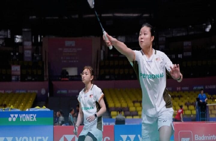 zu ya 2 - Wilayah.com.my Two female badminton players in white Petronas uniforms on a court; one prepares to spike the shuttle while the other watches closely.