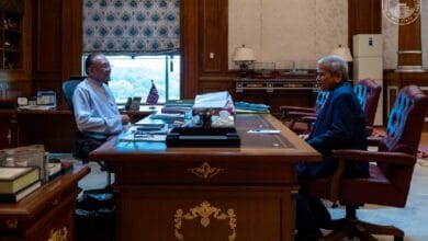 ahmad badri - Wilayah.com.my Two men in a formal government office sit across a large wooden desk, discussing papers.
