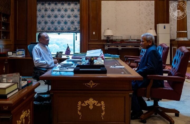 ahmad badri - Wilayah.com.my Two men in a formal government office sit across a large wooden desk, discussing papers.