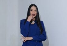 ain edruce - Wilayah.com.my Woman with long dark hair wearing a royal blue blazer poses with her hand near her chin, looking at the camera in a studio-like setting.