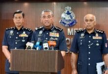 alzafny - Wilayah.com.my Three senior police officers in dark blue uniforms stand at a podium with microphones during a press briefing, Malaysia police emblem visible on the backdrop.