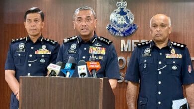 alzafny - Wilayah.com.my Three senior police officers in dark blue uniforms stand at a podium with microphones during a press briefing, Malaysia police emblem visible on the backdrop.