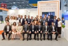 Group portrait of ARCTECH staff at a trade show booth, standing and sitting in front of a sign reading Global Leader in Solar Tracking Shipments.