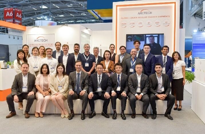 Group portrait of ARCTECH staff at a trade show booth, standing and sitting in front of a sign reading Global Leader in Solar Tracking Shipments.