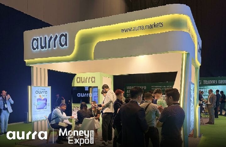 aurra 2 - Wilayah.com.my Aurra Markets booth at a Money Expo with a curved, yellow-lit display and people networking nearby.