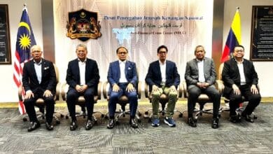 azam - Wilayah.com.my Six men in suits seated in a row for a formal group photo in a government office, with Malaysian and Philippine flags on either side and a crest on the wall behind.
