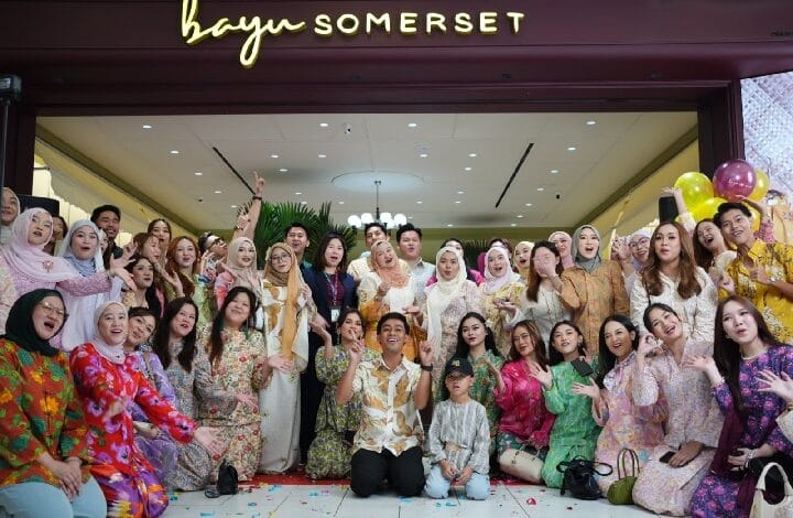 bayu somerset 2 - Wilayah.com.my Large group of people in colorful traditional outfits posing together for a group photo in front of a Bayu Somerset storefront, celebrating together.