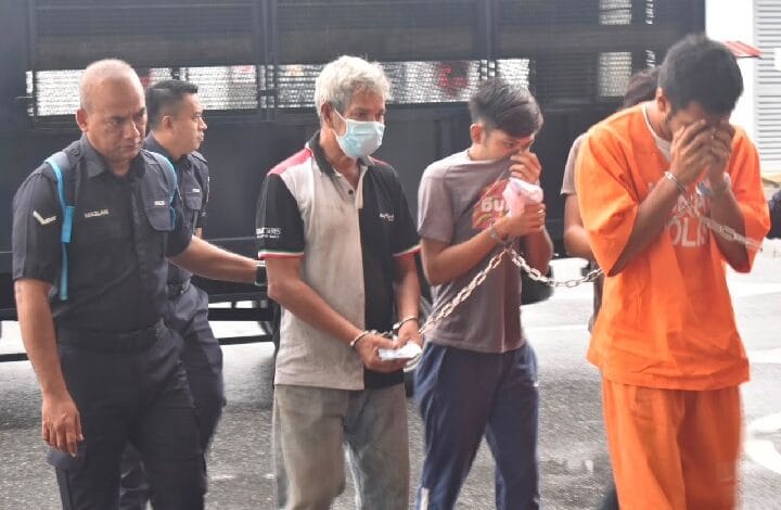 court - Wilayah.com.my Security officers escort two detainees in orange jumpsuits; one detainee covers face as they walk forward with chained hands nearby a masked man and other officer nearby.