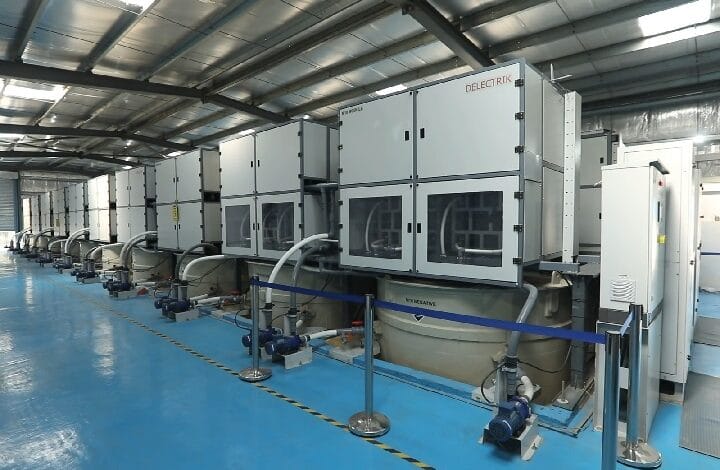 delectrik 2 - Wilayah.com.my Row of large gray industrial machines connected by hoses in a blue-floored factory hall.
