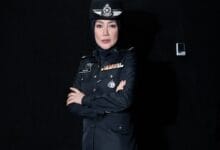 era fazira2 - Wilayah.com.my Female police officer in a dark formal uniform with medals, wearing a hijab, arms crossed against a black background.