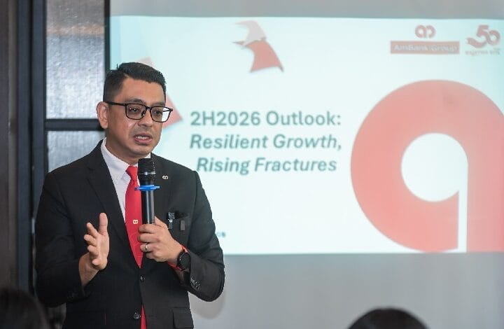 firdaos rosli 2 - Wilayah.com.my Professional man in a dark suit and red tie speaks into a handheld microphone during a presentation, with a slide behind him reading '2H2026 Outlook: Resilient Growth, Rising Fractures'.