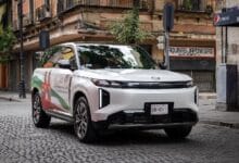 gac - Wilayah.com.my White SUV with colorful promotional wrap parked on a cobblestone city street in front of storefronts.