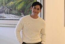 hun haqeem 2 - Wilayah.com.my Man in a white knit sweater smiles at the camera indoors, with a landscape painting on the wall behind him.
